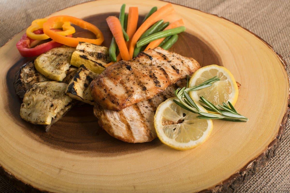 Grilled chicken breast with roasted vegetables and lemon on a wooden board