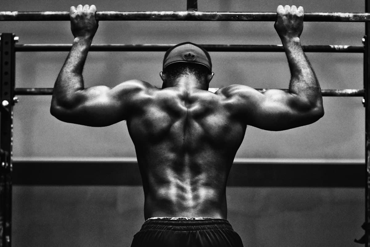 A man doing a pull-up, seen from behind, in black and white